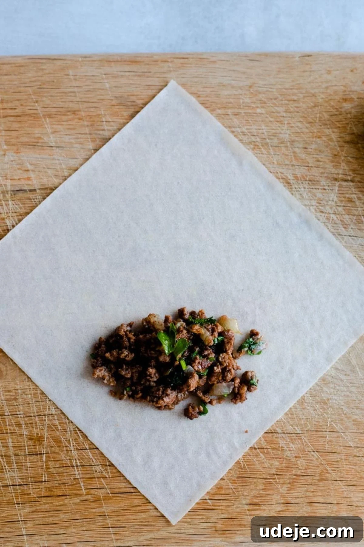 Your Guide to Authentic Homemade Sambousek 12 a square spring roll wrapper on a wooden board, with ground beef filling inside