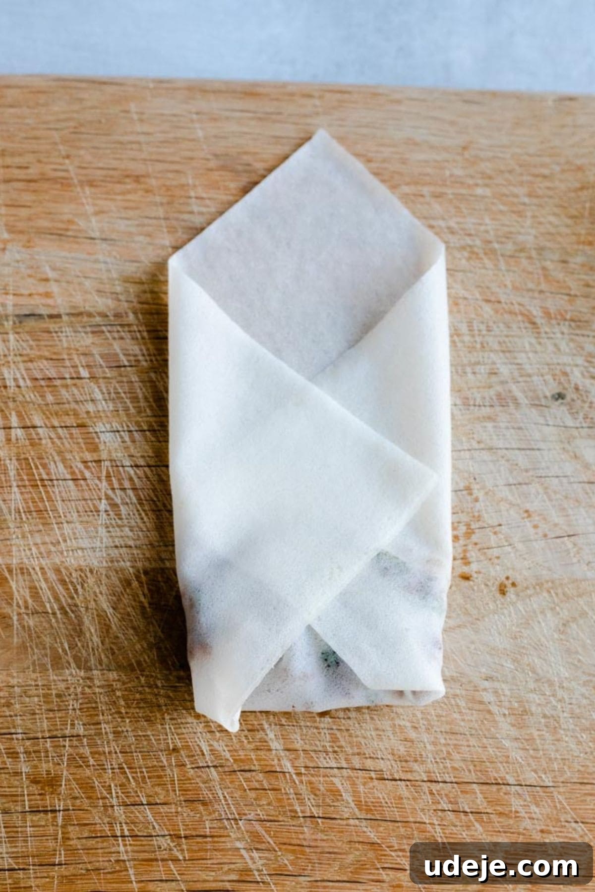 Your Guide to Authentic Homemade Sambousek 15 a square spring roll wrapper on a wooden board, with ground beef filling inside, being rolled