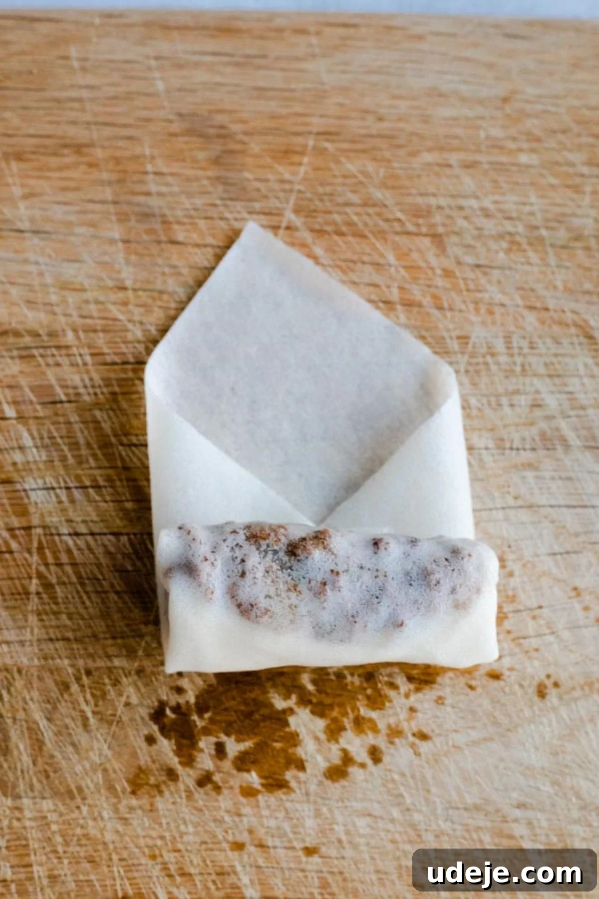 Your Guide to Authentic Homemade Sambousek 16 a square spring roll wrapper on a wooden board, with ground beef filling inside, being rolled into a cylinder shape