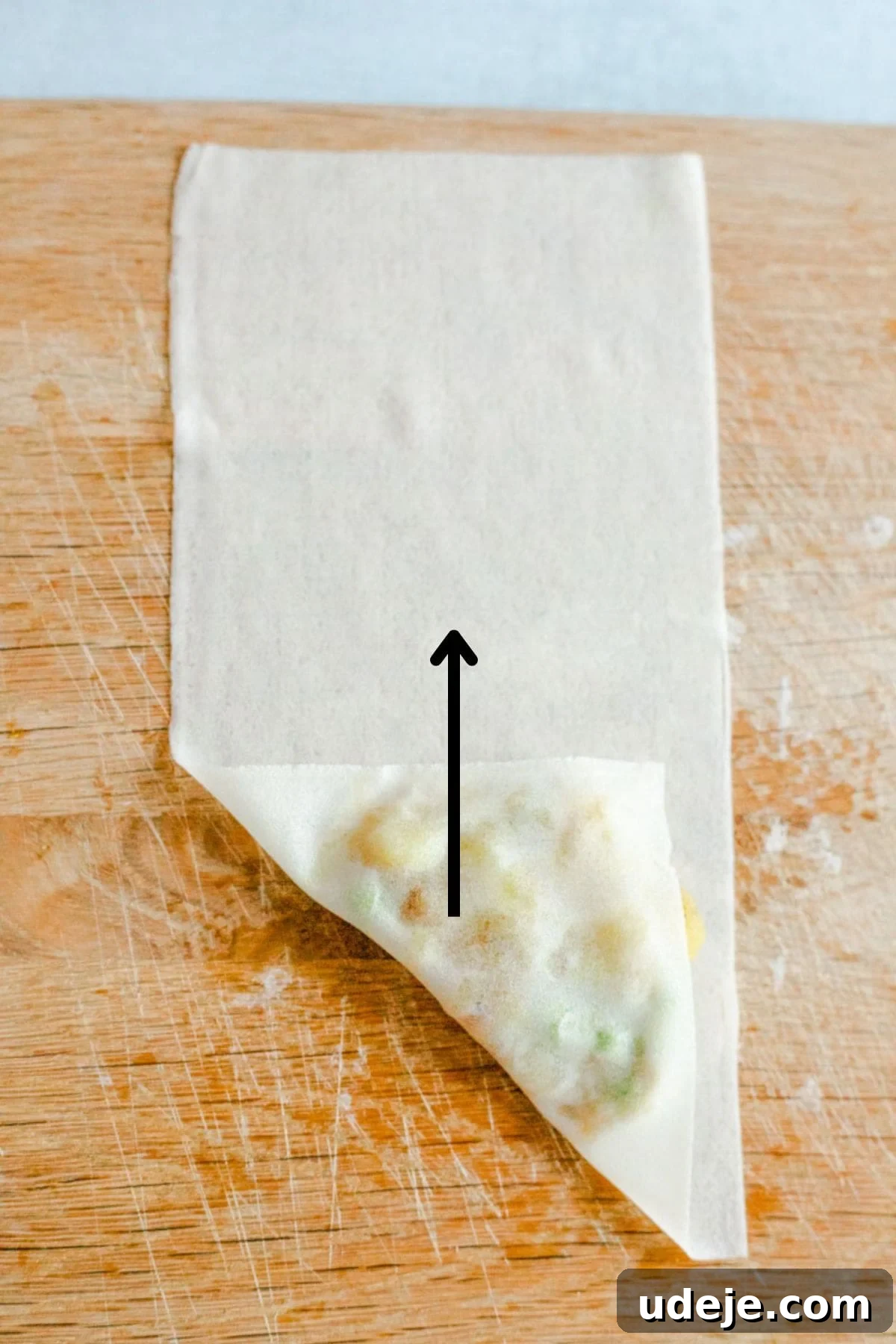 Your Guide to Authentic Homemade Sambousek 19 a square spring roll wrapper on a wooden board, with a potato and pea filling, being wrapped in triangle shape