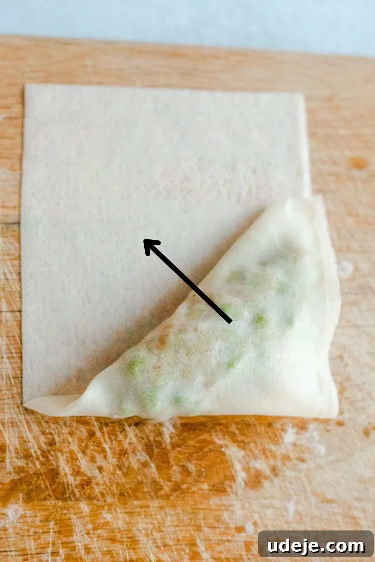 Your Guide to Authentic Homemade Sambousek 20 a square spring roll wrapper on a wooden board, with a potato and pea filling, being wrapped in triangle shape