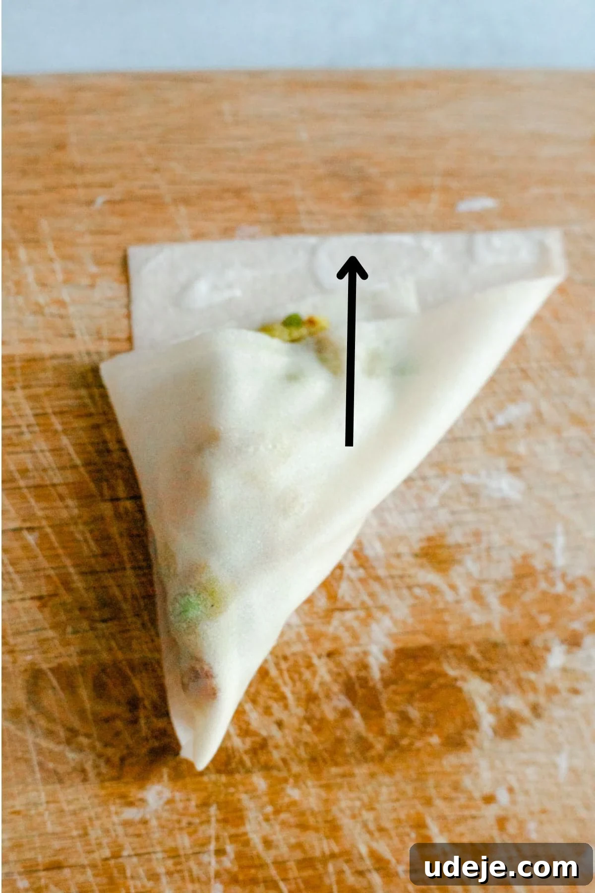 Your Guide to Authentic Homemade Sambousek 21 a square spring roll wrapper on a wooden board, with a potato and pea filling, being wrapped in triangle shape