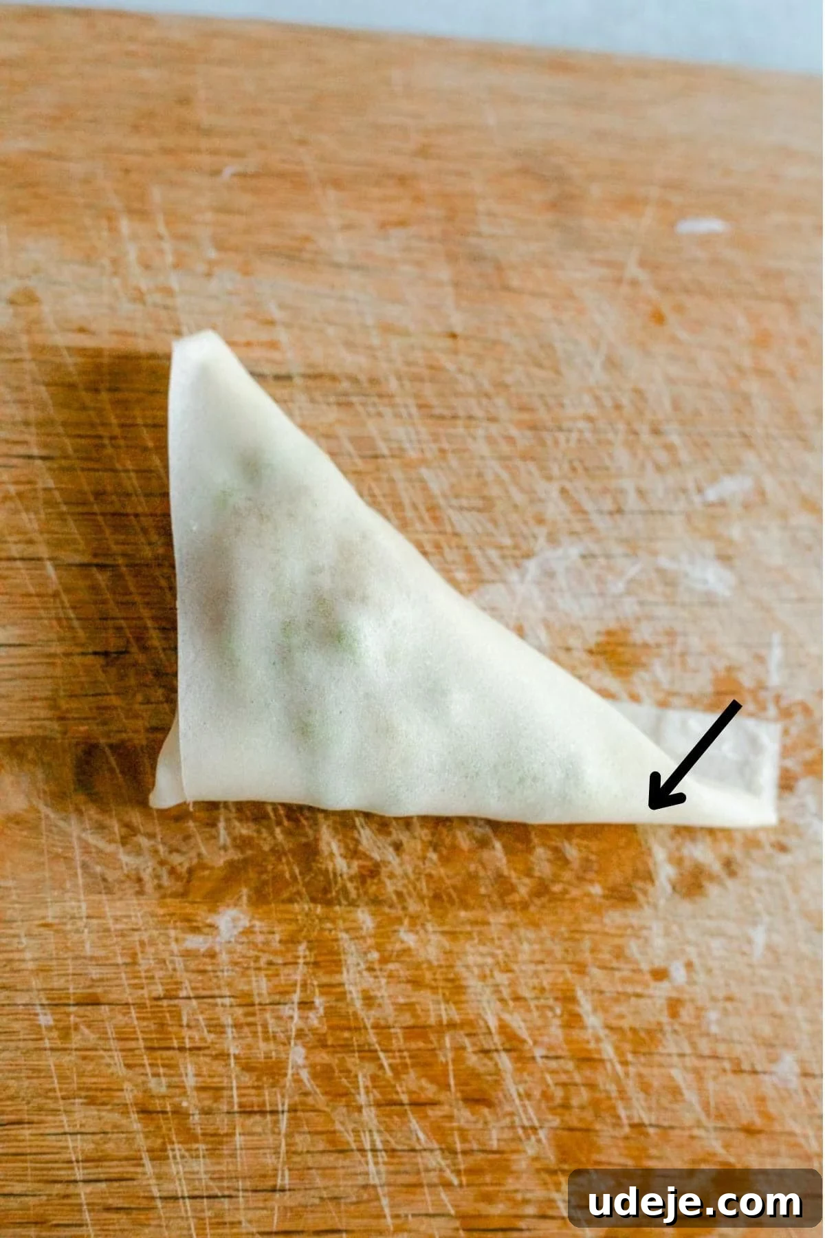 Your Guide to Authentic Homemade Sambousek 22 a square spring roll wrapper on a wooden board, with a potato and pea filling, being wrapped in triangle shape