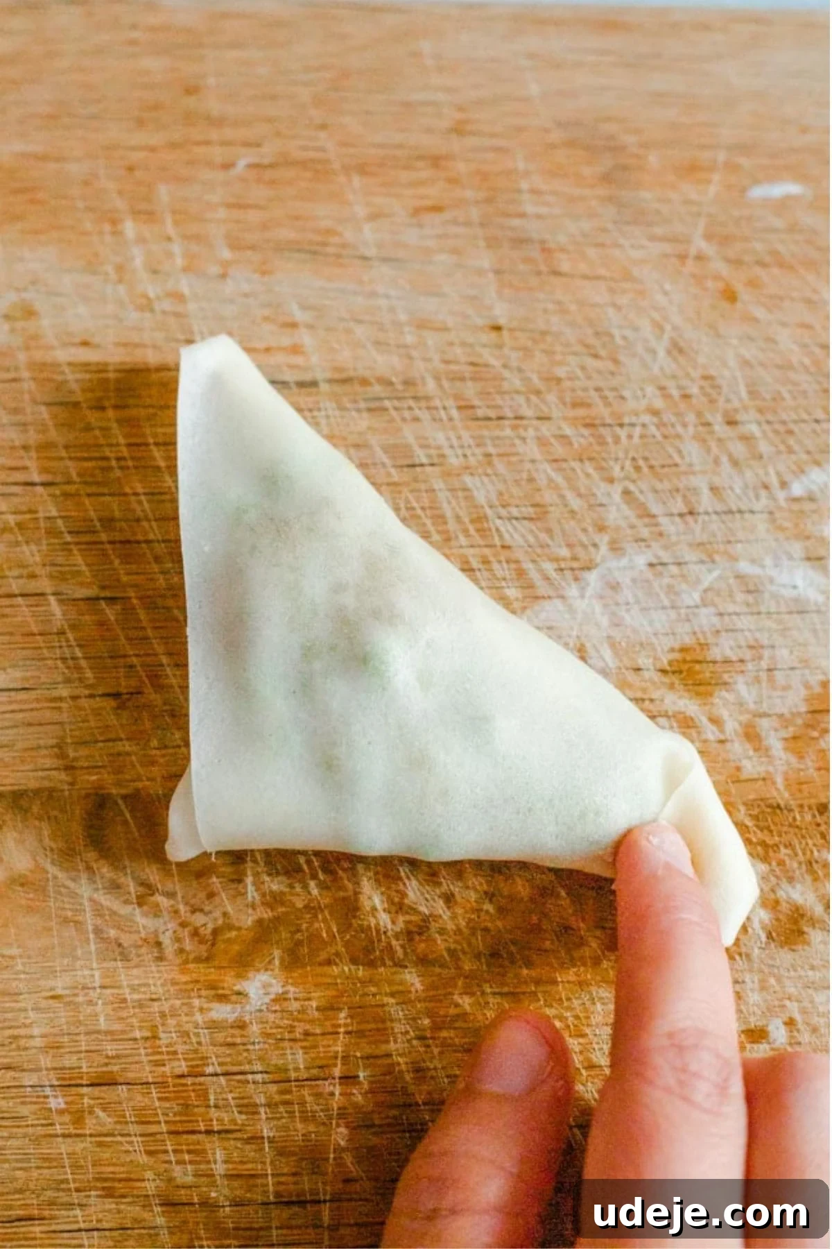 Your Guide to Authentic Homemade Sambousek 23 a square spring roll wrapper on a wooden board, with a potato and pea filling, being wrapped in triangle shape