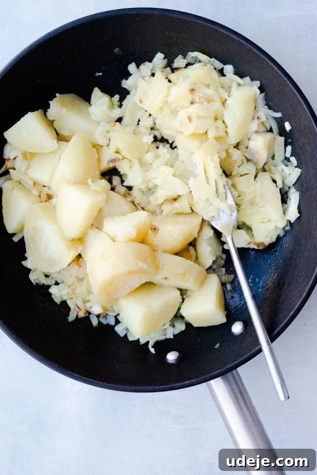 Your Guide to Authentic Homemade Sambousek 8 cubes of potato in a black pan being mashed by a fork