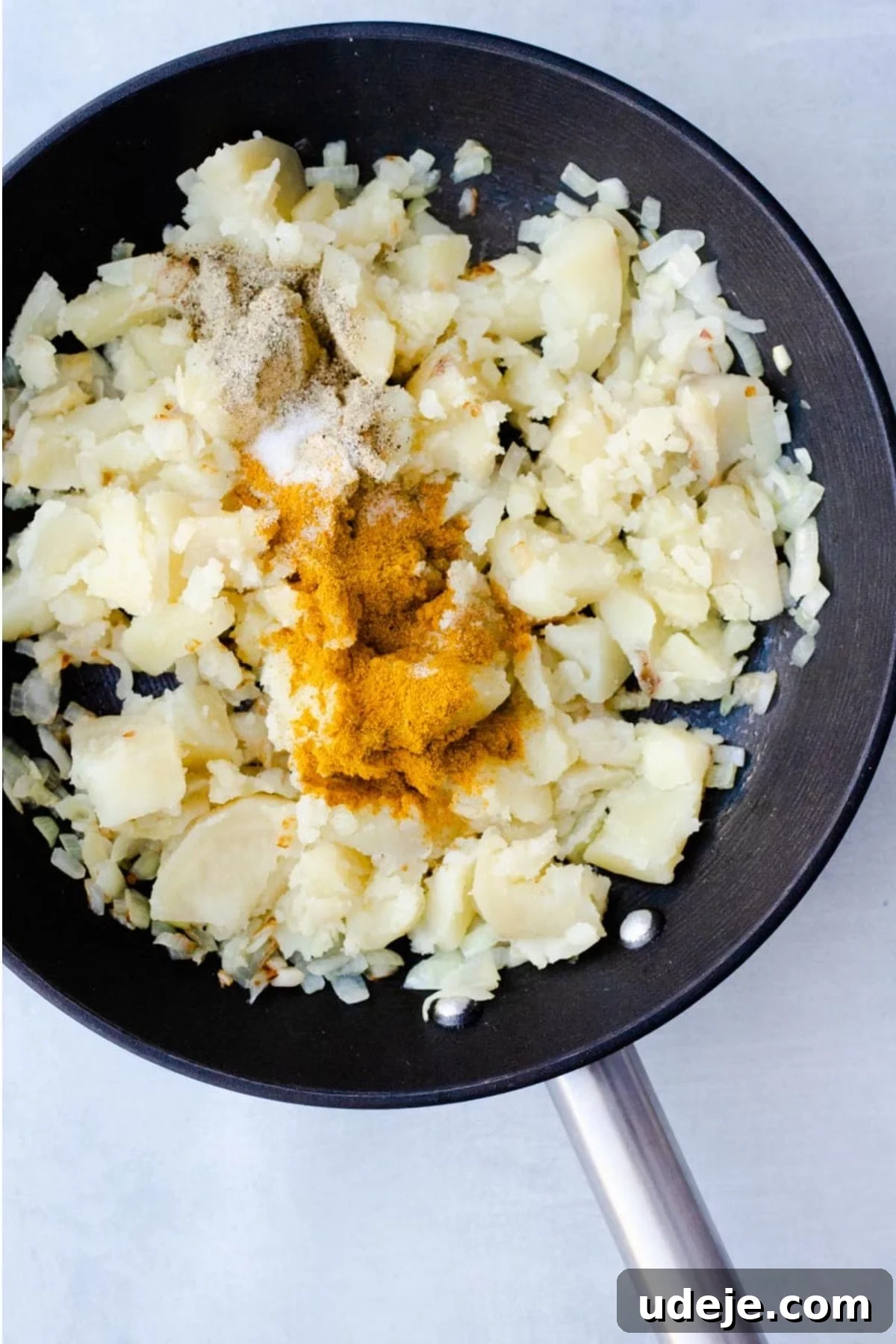 Your Guide to Authentic Homemade Sambousek 9 cubes of potato mashed in a black pan, with spices on top