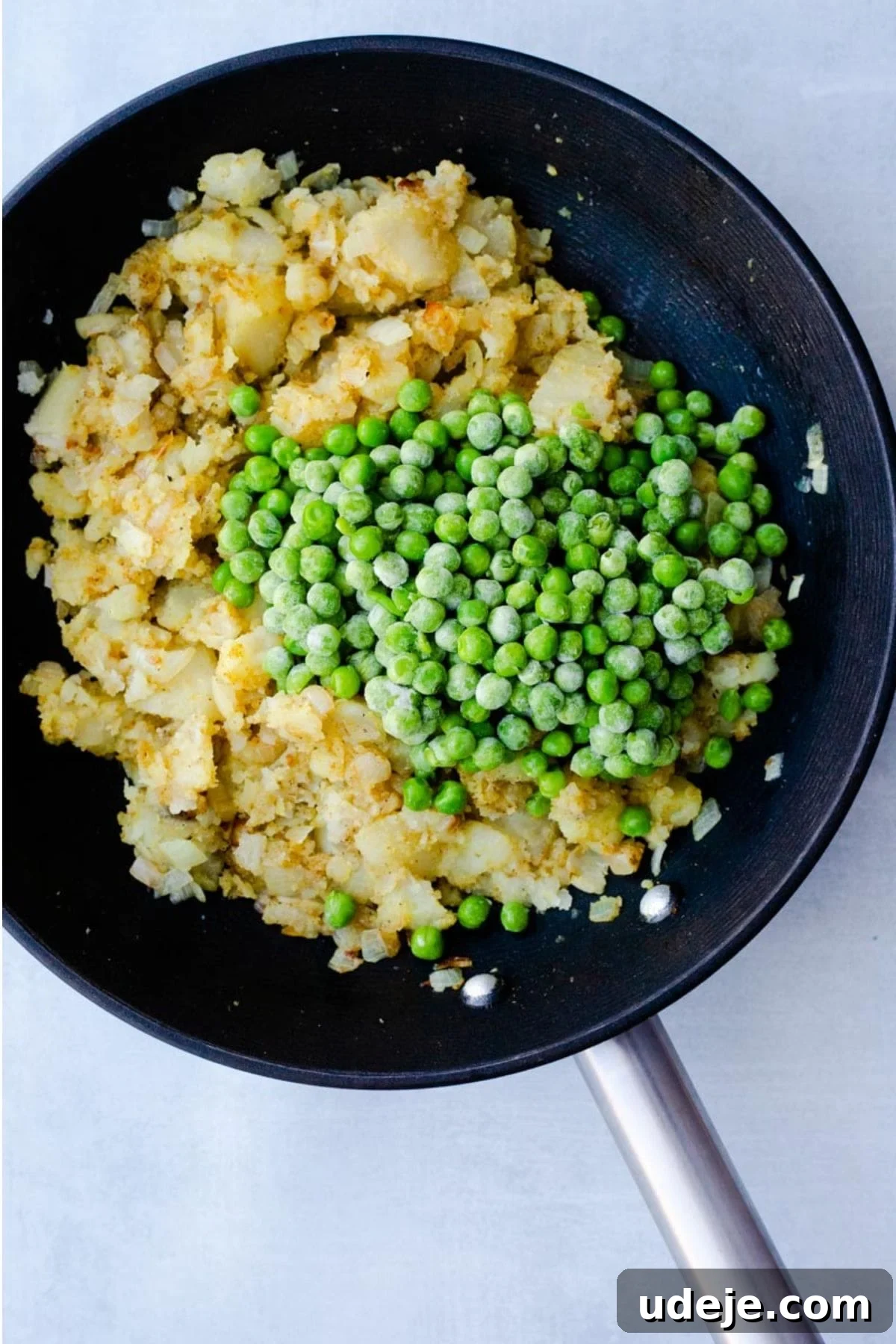 Your Guide to Authentic Homemade Sambousek 10 potatoes being mashed in a pan with onions spices and frozen pees