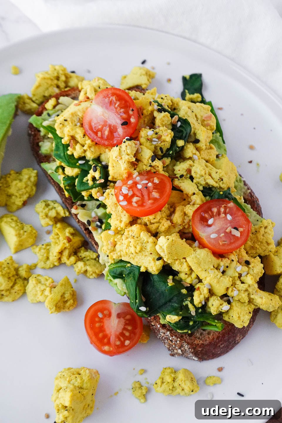 Next-Level Tofu Scramble 3 close up of vegan tofu scramble served on sourdough toast with fresh spinach, cherry tomatoes, and mashed avocado for a healthy and flavorful breakfast.