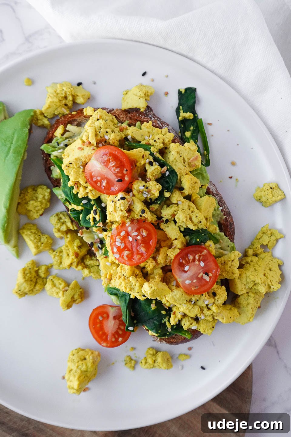 Next-Level Tofu Scramble 5 Vegan tofu scramble served on sourdough toast with fresh spinach, cherry tomatoes, and mashed avocado for a healthy and flavorful breakfast.