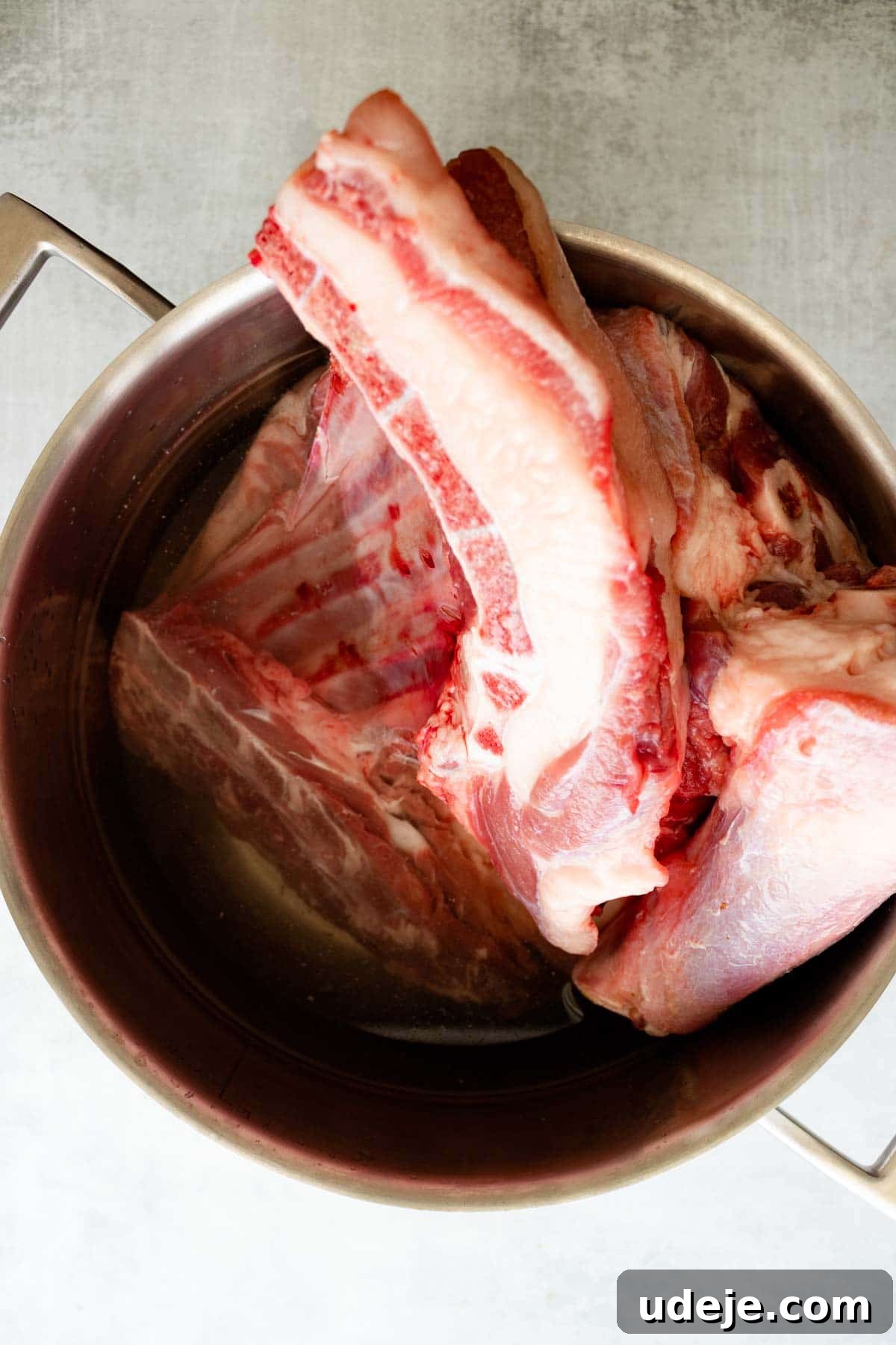 Authentic Iraqi Quzi: Slow-Cooked Lamb on Aromatic Rice 6 Large, raw lamb bones for Quzi are placed in a metal pot filled with water, viewed from above on a light-colored surface.