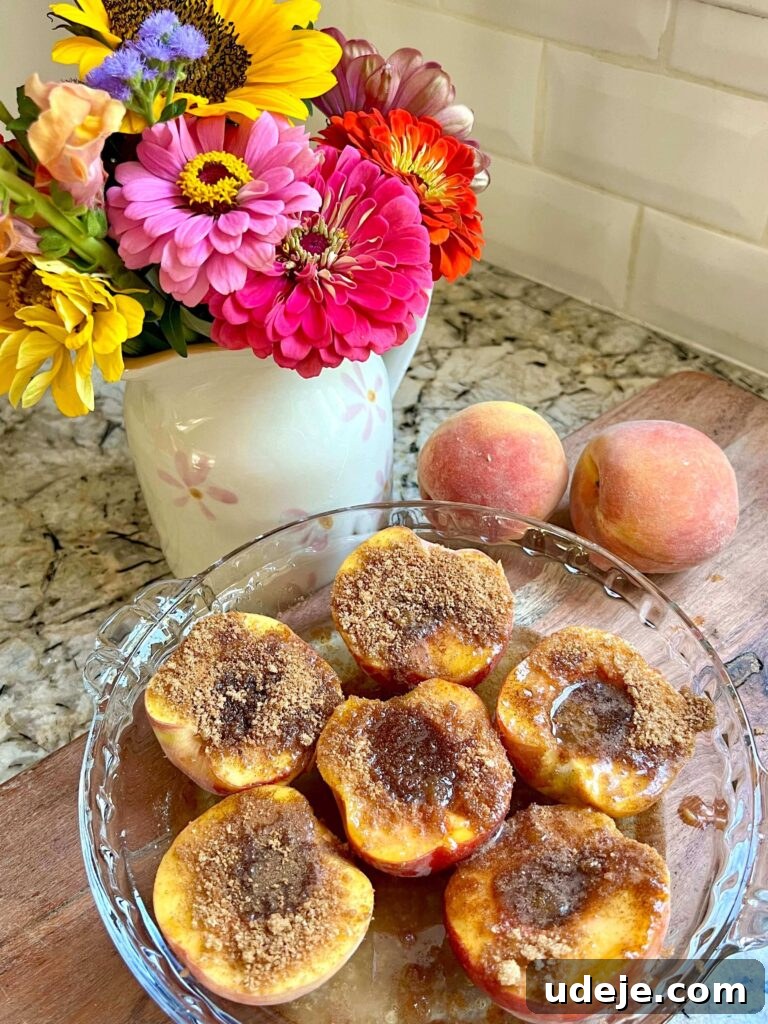 Golden Baked Peaches 4 Two halves of baked peaches resting in a white baking dish, glistening with a cinnamon-sugar topping.