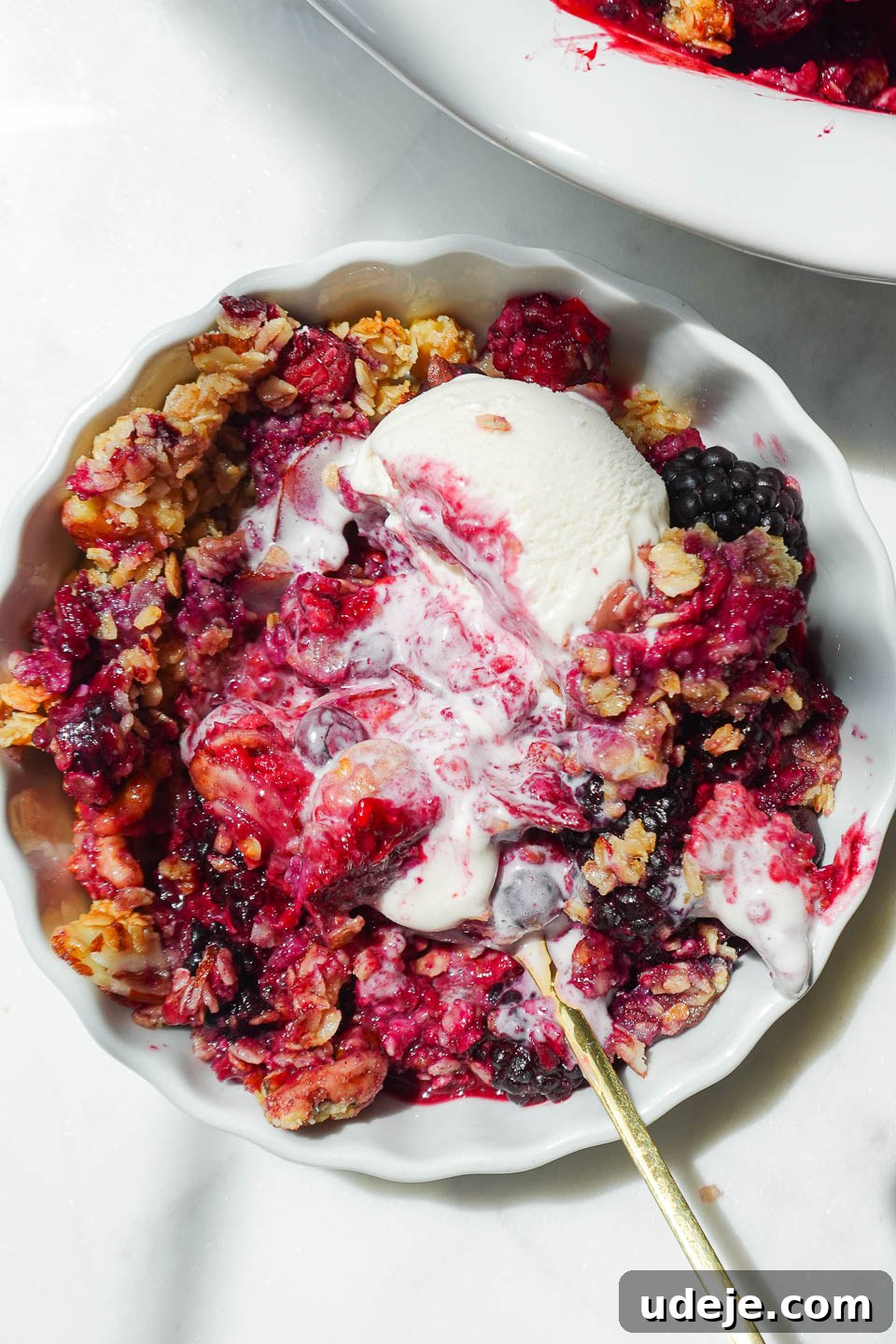 Wholesome Berry Crumble 3 Close up of a spoonful of vegan and gluten-free healthy berry crisp with creamy vegan vanilla ice cream.