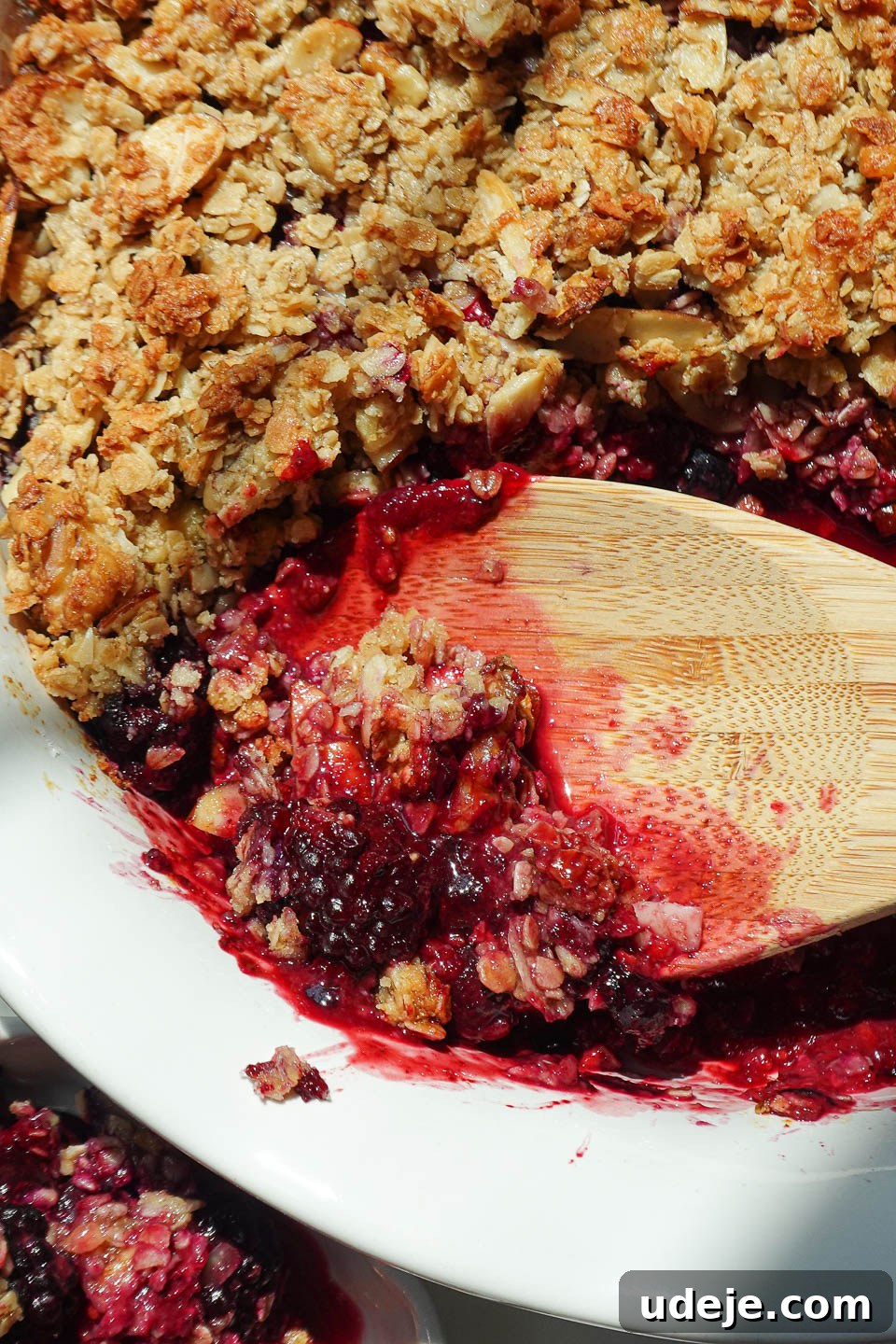 Wholesome Berry Crumble 4 Healthy berry crisp made with a mix of berries and a golden nutty topping, served with a wooden spoon.