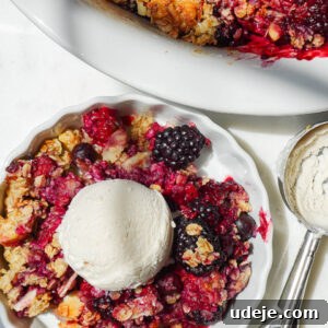 overhead shot of healthy berry crisp in a bowl topped with a scoop of vegan vanilla ice cream