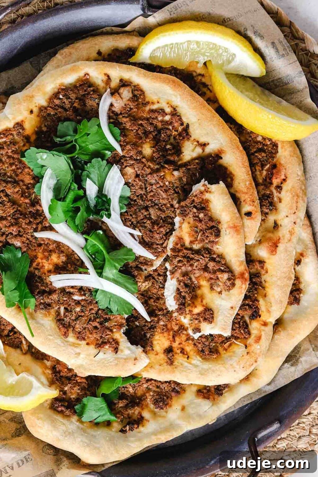 Lahm Bi Ajeen Savory Middle Eastern Flatbread 19 Lahm Bi Ajeen piled on a dark coloured tray with parchment, garnished with lemon wedges, parsley and onion slices