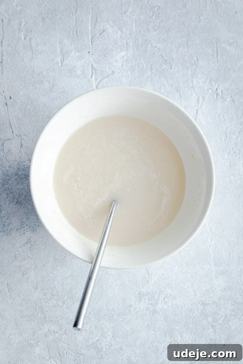 Lahm Bi Ajeen Savory Middle Eastern Flatbread 4 a mixture of yeast and water in a white bowl, with a spoon inside