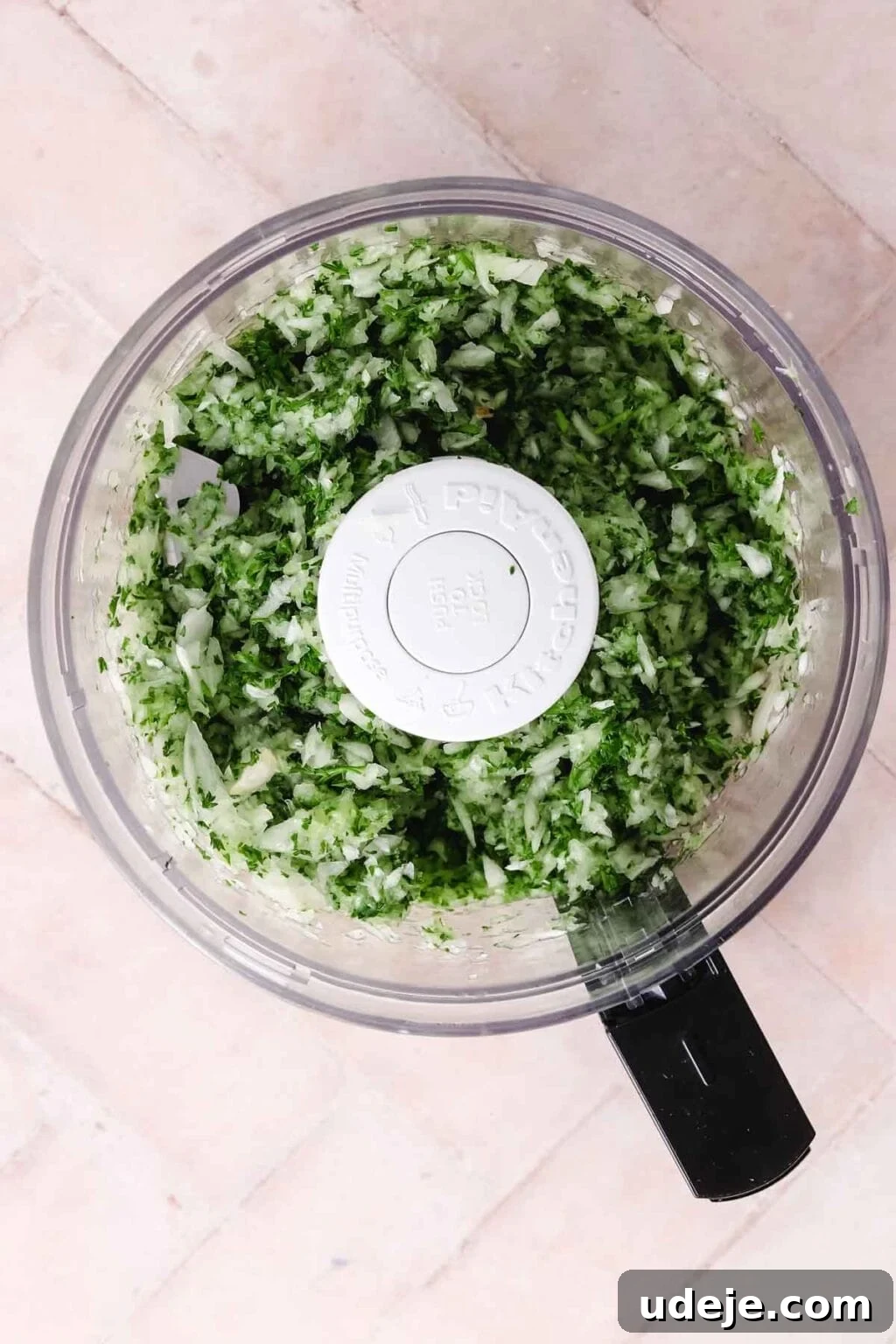 Lahm Bi Ajeen Savory Middle Eastern Flatbread 8 onions and parsley in a food processor that have been processed into small pieces on a light pink tiled background
