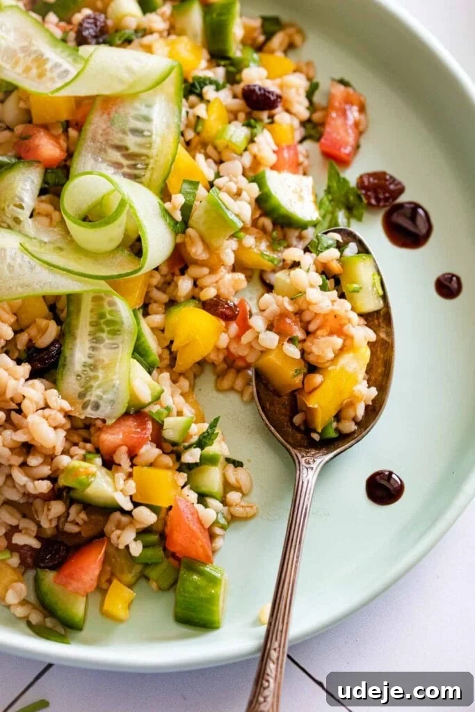 Crisp Bulgur Salad: Effortless & Delicious 3 A plate of fresh Bulgur Salad with diced cucumber, yellow pepper, tomato, parsley, and raisins, garnished with cucumber ribbons. A spoon rests on the plate next to this colorful and vibrant salad.
