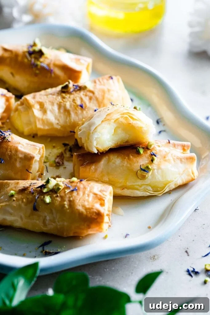 Crunchy and Delicious Znoud El Sit (Lady Fingers) A beautifully arranged plate showcasing several golden-brown Znoud El Sit (Lady Fingers) pastries, glistening with sugar syrup and adorned with finely chopped vibrant green pistachios, ready to be enjoyed.