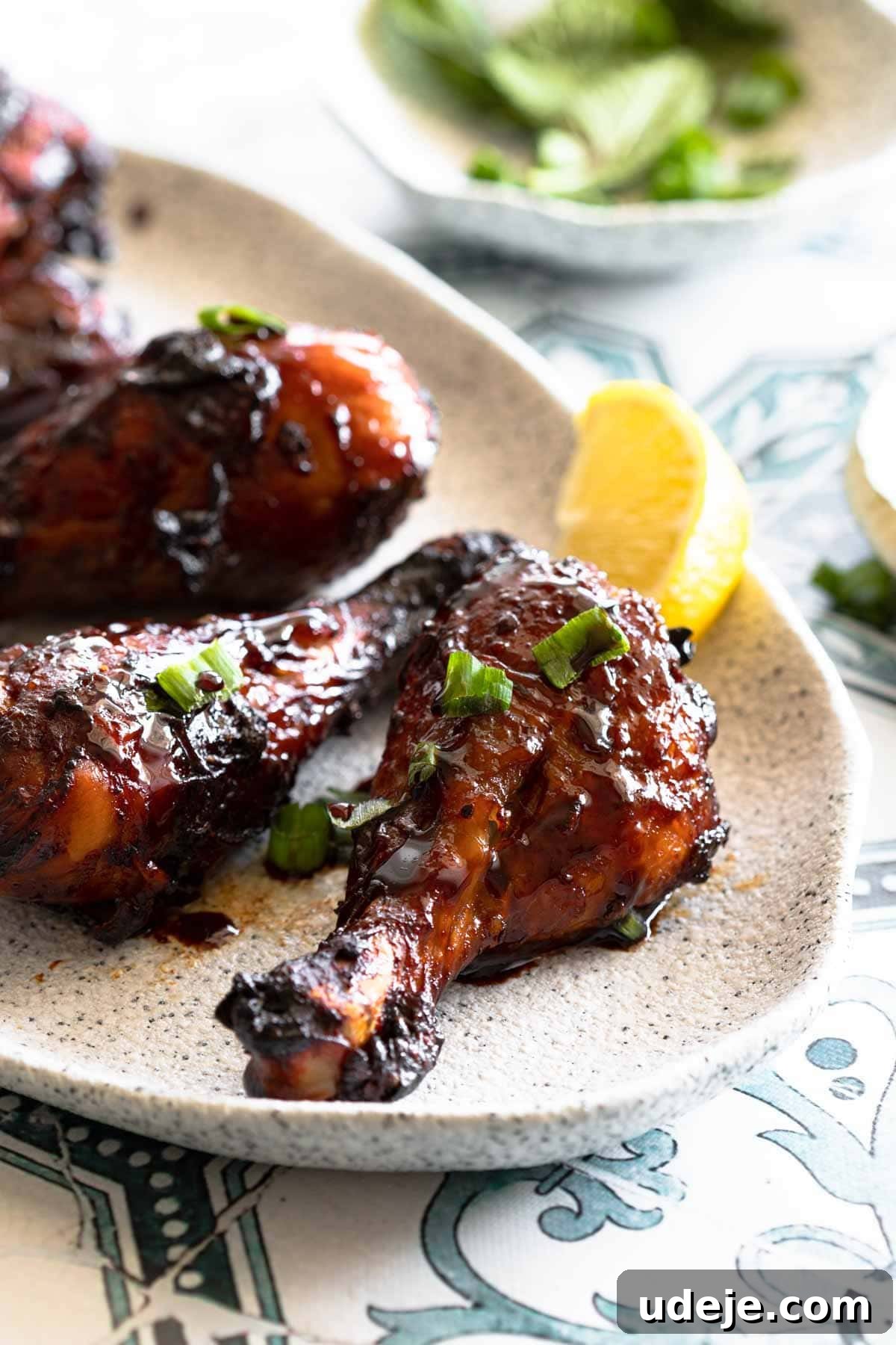 Sticky Pomegranate Air Fryer Drumsticks 2 Chicken drumsticks glazed in pomegranate sauce served on a plate with fresh herbs and pomegranate arils