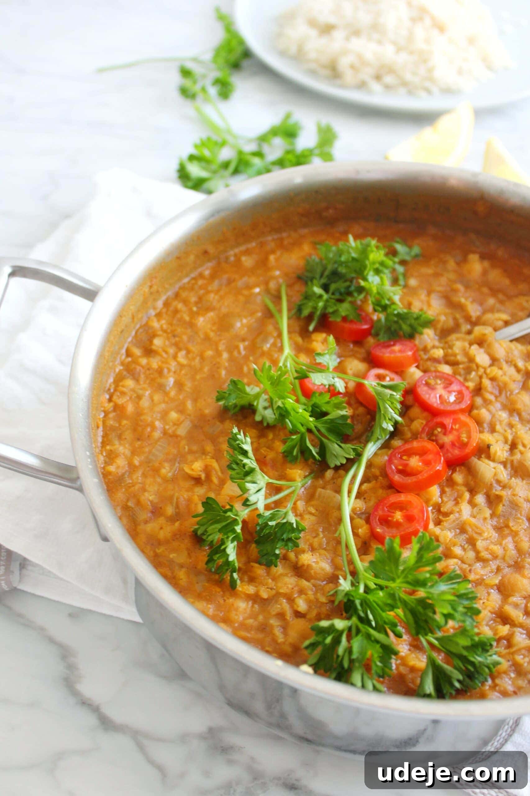 Golden Coconut Lentil and Chickpea Curry 2 A pot of vibrant red lentil and chickpea coconut curry, garnished with fresh cilantro and a swirl of coconut cream, served with fluffy basmati rice and lime wedges on a rustic wooden table.