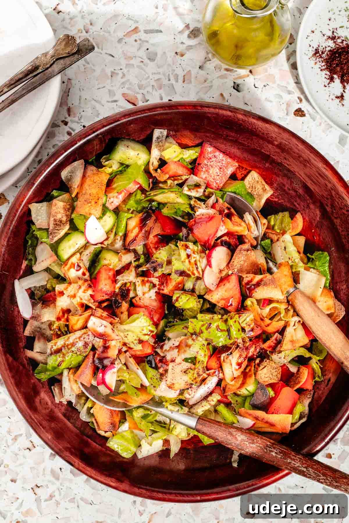 Signature Restaurant Fattoush 8 A fattoush salad in a wooden salad bowl, which includes chopped lettuce, cucumber, red pepper, radish and tomatoes, all drizzled with salad dressing. Olive oil and sumac in the top right corner.