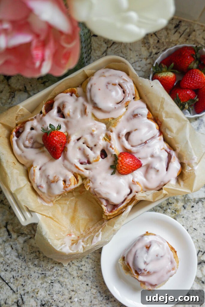 Plant-Based Strawberry Swirls 8 Close-up of a single Vegan Strawberry Roll topped with generous cream cheese icing and a fresh strawberry slice.