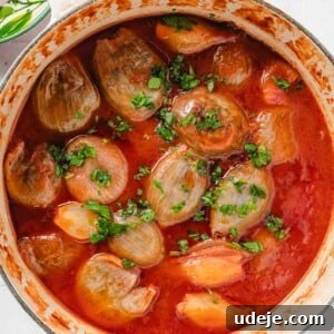 Hearty Beef-Stuffed Onions 16 White handled pot with stuffed onions in a tomato broth and chopped parsley on top on a blue and white tiled background with a bowl of chopped parsley at the side.