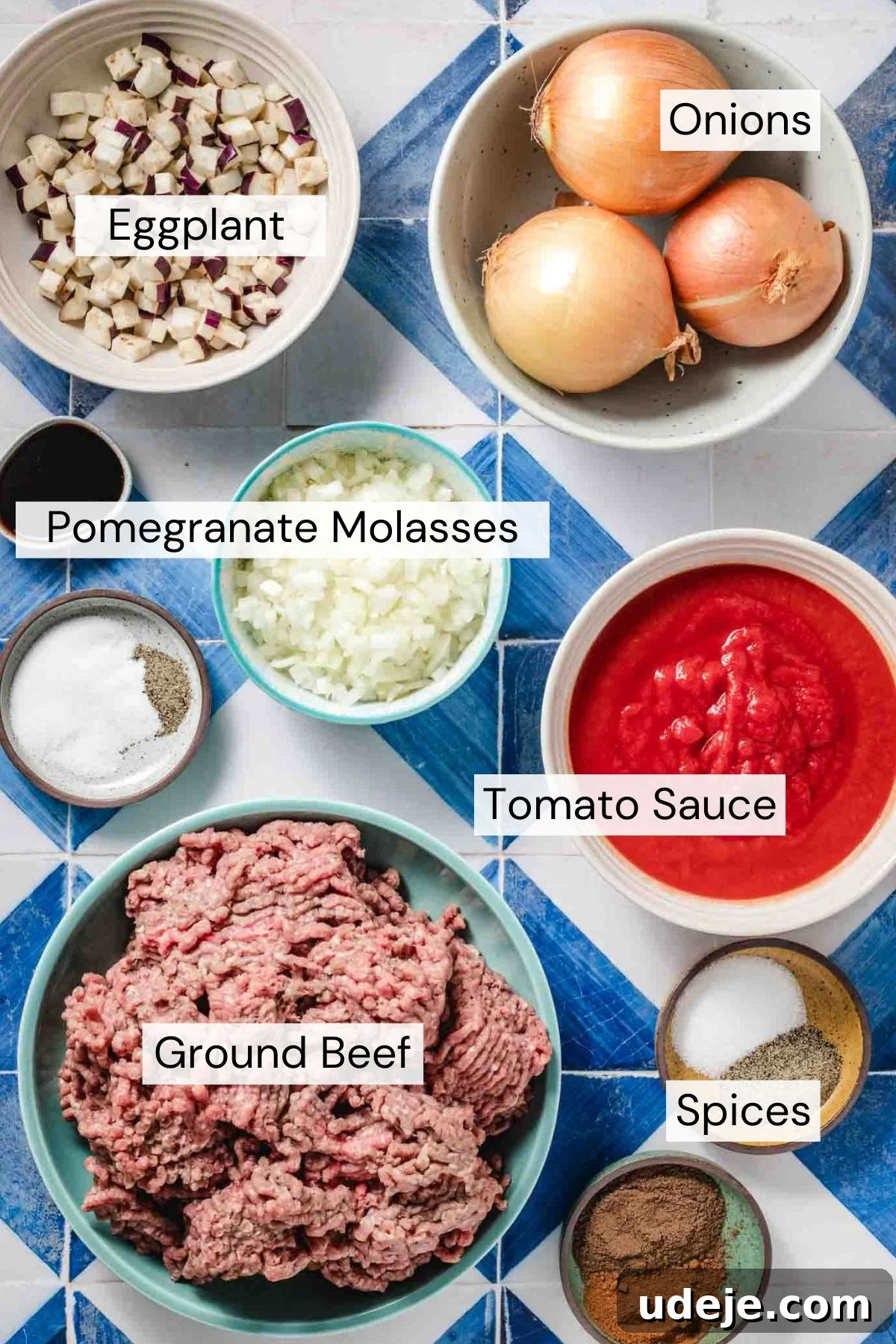 Hearty Beef-Stuffed Onions 3 Bowls filled with labeled ingredients on a blue tile surface: diced eggplant, whole onions, pomegranate molasses, chopped onions, tomato sauce, ground beef, and assorted spices.