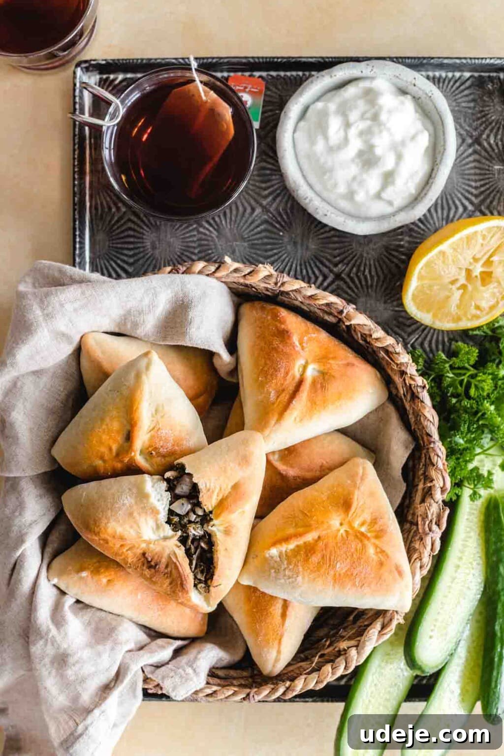 Authentic Homemade Spinach and Cheese Fatayer 2 Spinach fatayer served in a bread basket alongside cucumbers, parsley, lemon, yogurt and black tea