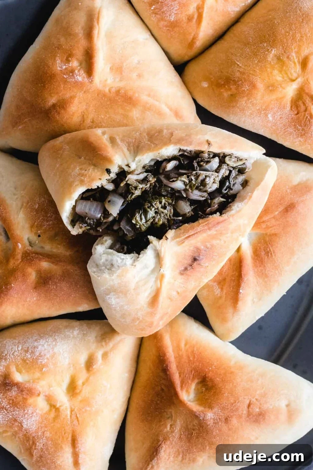 Authentic Homemade Spinach and Cheese Fatayer 15 Spinach fatayer on a platter with the top one open to reveal spinach and onion stuffing