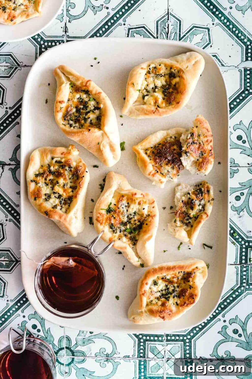 Authentic Homemade Spinach and Cheese Fatayer 3 Cheese fatayer served on a white platter with a cup of black tea