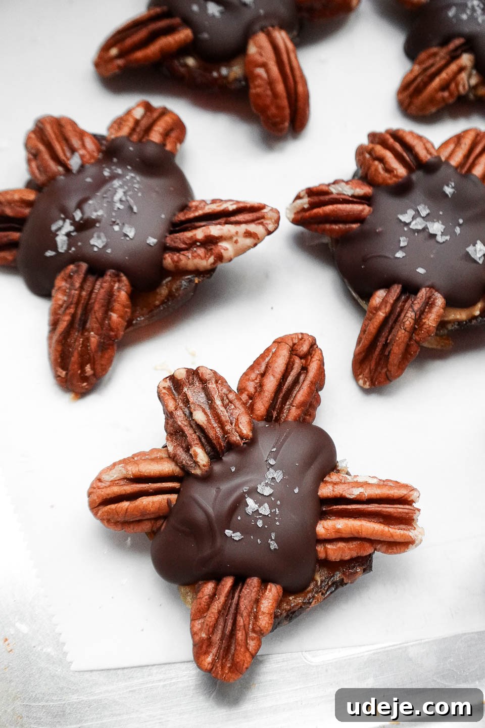 Easy 4-Ingredient Healthy Chocolate Turtles 4 Close-up of three vegan chocolate turtles generously sprinkled with flaky sea salt, arranged on a baking sheet, emphasizing the sweet and salty flavor profile.