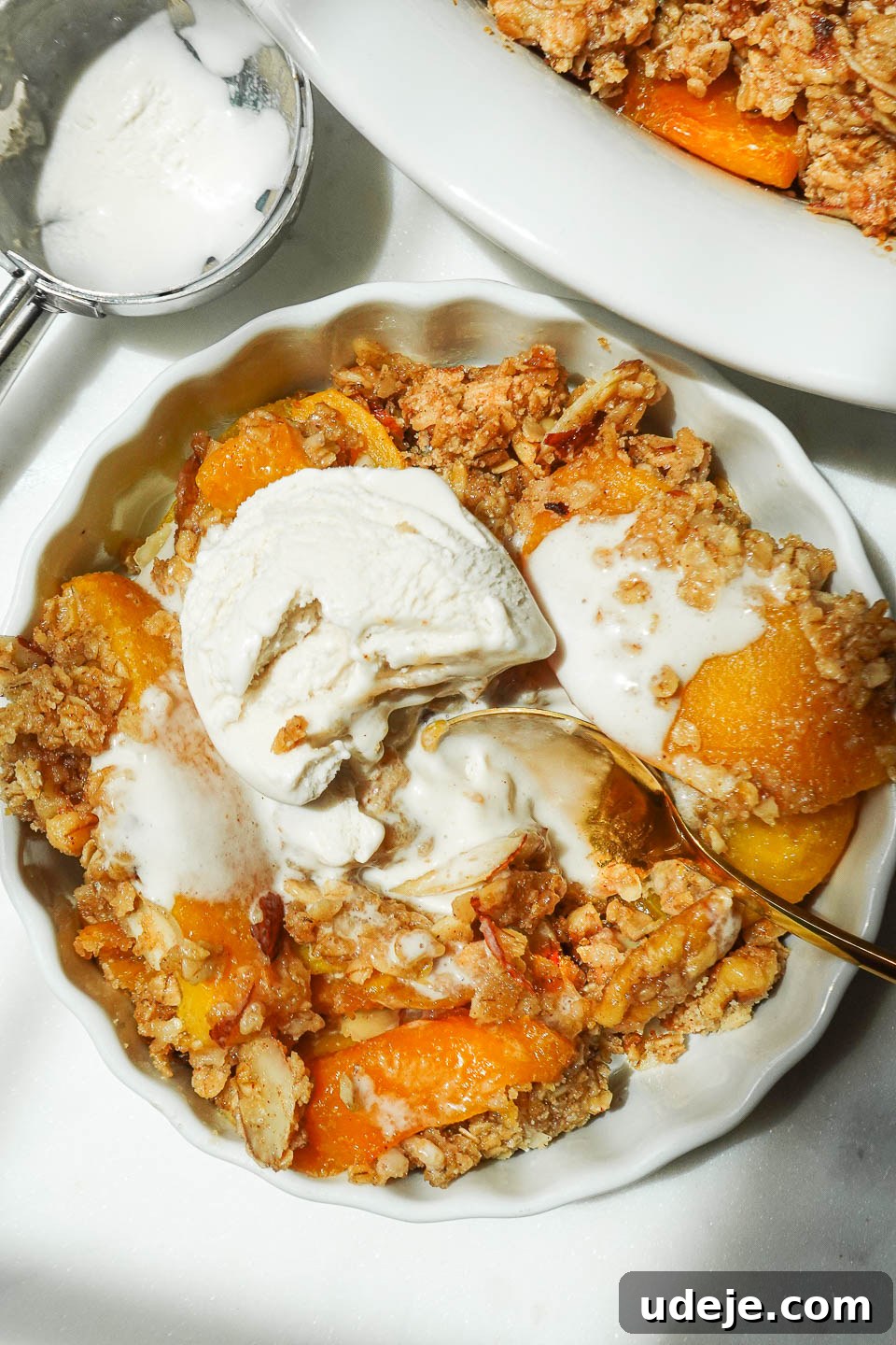 Wholesome Peach Crumble 2 A ramekin holding a warm serving of healthy peach crisp, topped with a scoop of vegan vanilla ice cream gently melting over the golden, nutty topping.