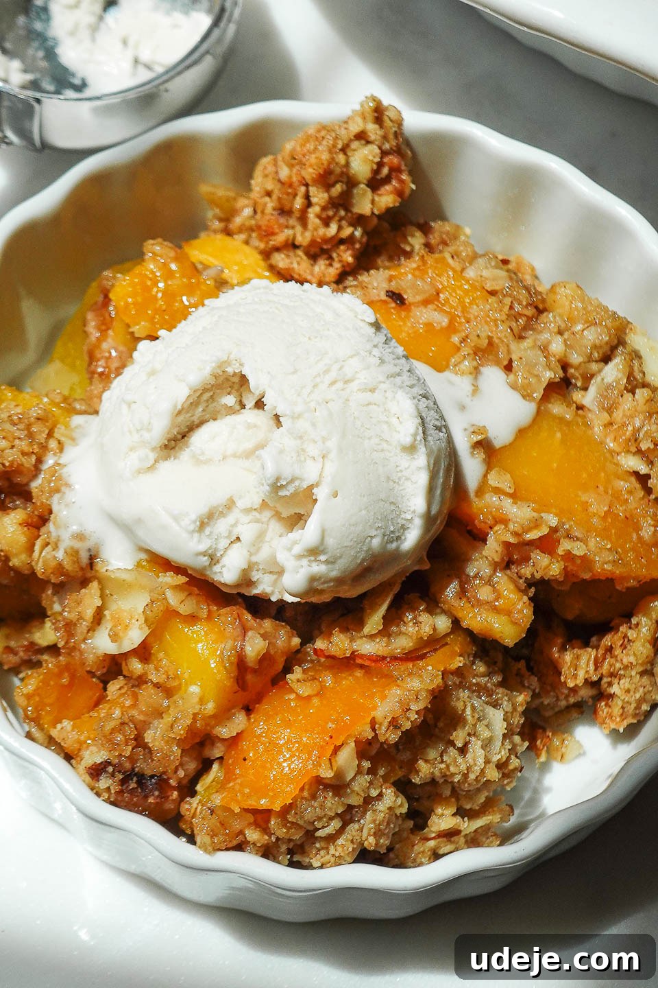 Wholesome Peach Crumble 3 Close-up shot of a serving of healthy vegan peach crisp, exquisitely topped with a generous scoop of vegan vanilla ice cream, creating a delightful contrast.