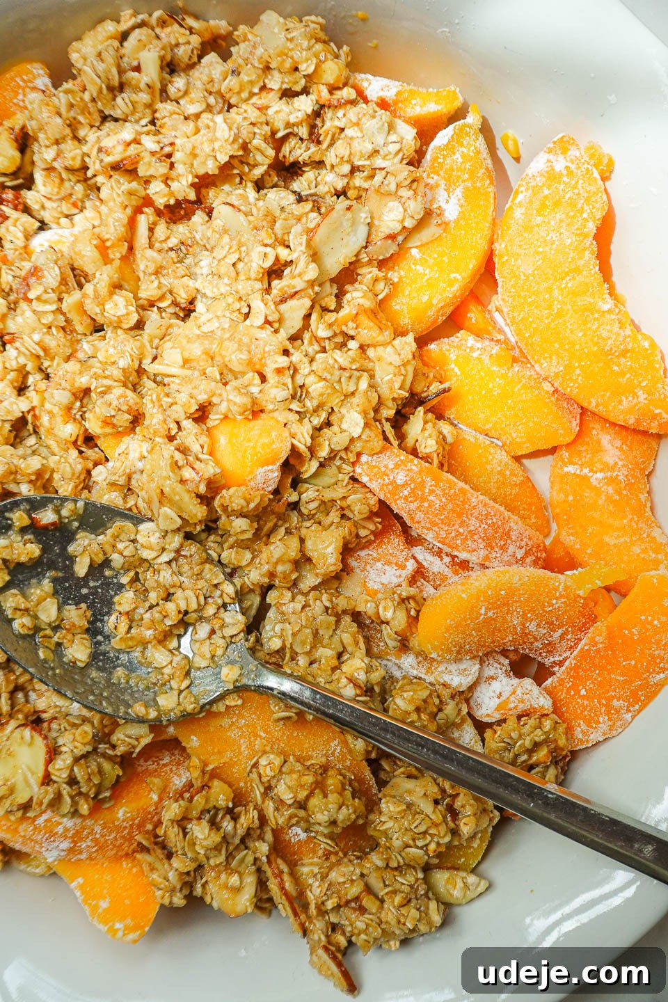 Wholesome Peach Crumble 7 The oat-almond crisp topping being meticulously sprinkled, ensuring even coverage over the sweet and spiced peach filling.
