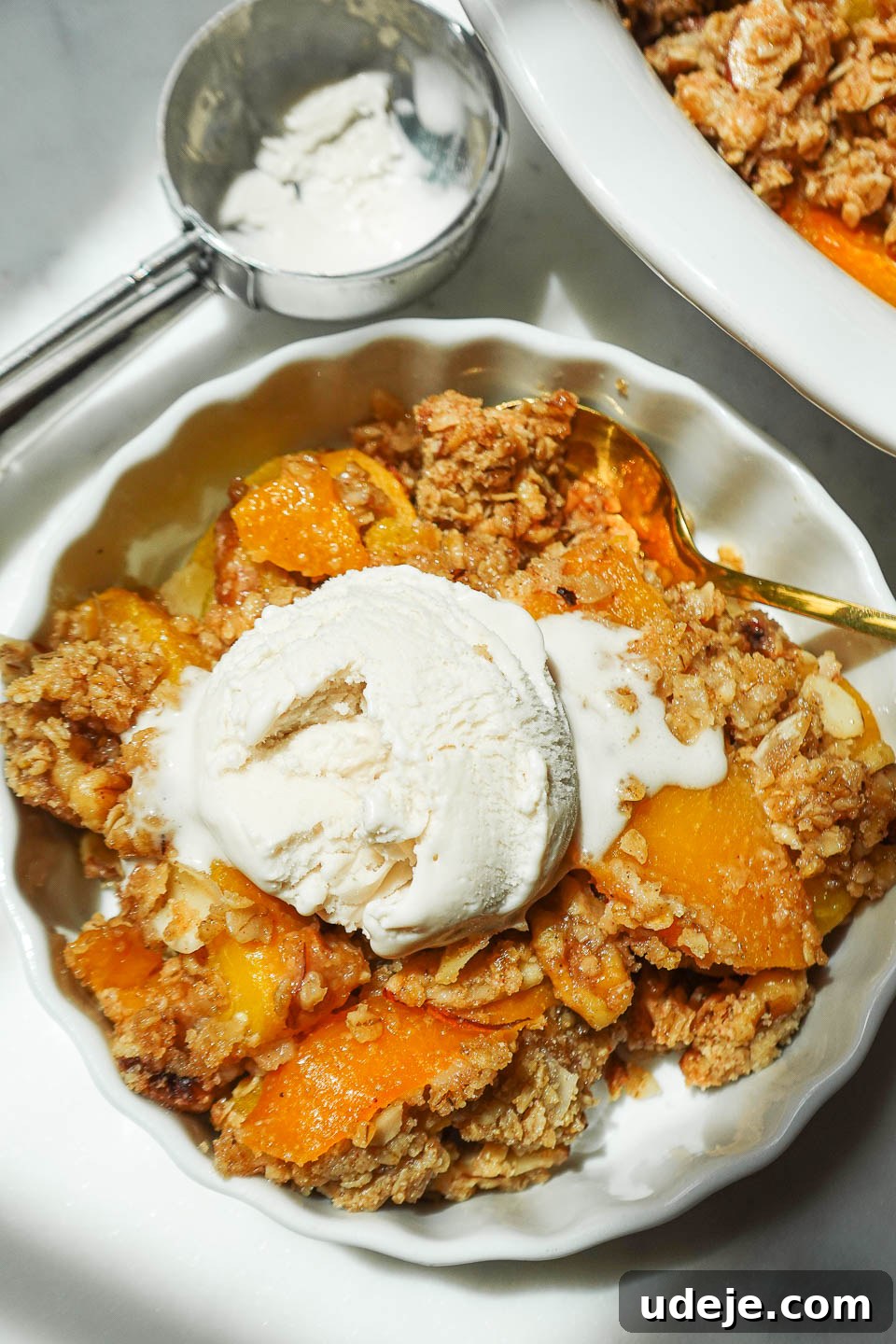 Wholesome Peach Crumble 8 An inviting overhead shot of freshly baked peach crisp, beautifully golden, adorned with a scoop of vegan vanilla ice cream.