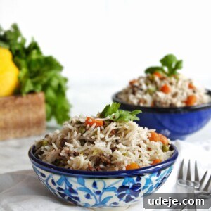 Two blue-patterned bowls filled with vibrant Instant Pot Keema Rice, garnished with fresh cilantro, resting on a white linen cloth. A fork and spoon are placed beside one bowl, with blurred green vegetables and a lemon in the background, suggesting a fresh, wholesome meal.