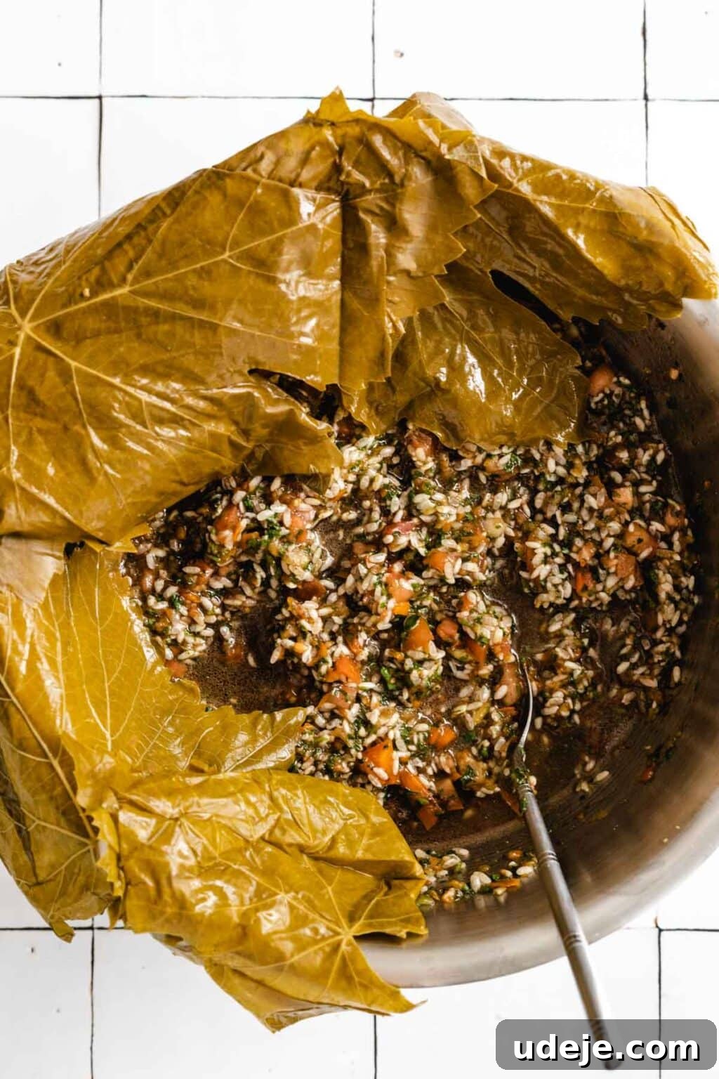 Authentic Yalanji Vegetarian Stuffed Grape Leaves 6 A bowl filled with a mixture of rice and vegetables for stuffing, with grape leaves draped around the sides, ready for the rolling process.