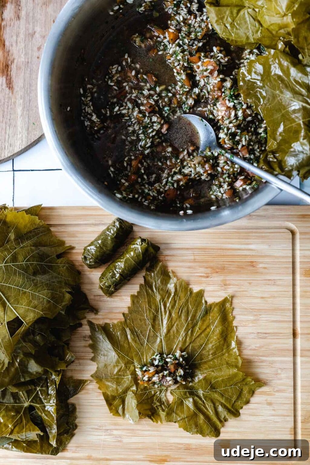 Authentic Yalanji Vegetarian Stuffed Grape Leaves 7 The process of rolling grape leaves, showing a bowl of stuffing and one leaf spread flat on a cutting board, ready to be filled and rolled.