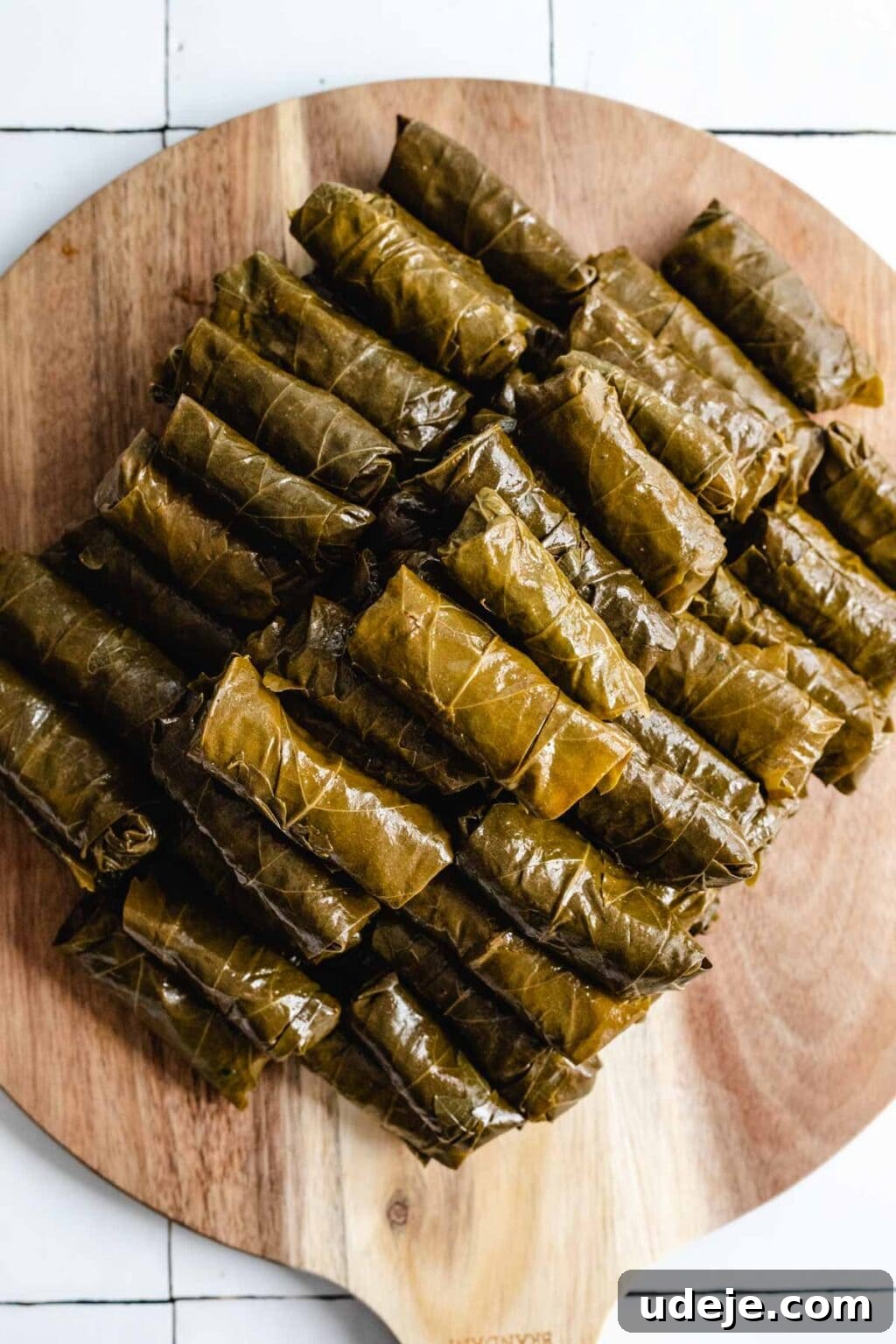 Authentic Yalanji Vegetarian Stuffed Grape Leaves 9 A pile of perfectly stuffed and rolled grape leaves arranged on a circular wooden board, ready for cooking.