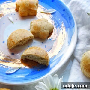 A blue and white plate with flower-shaped biscuits, one broken in half, surrounded by white daisies on a light surface with a white cloth, inviting you to try this Iraqi Soda Cookies recipe.