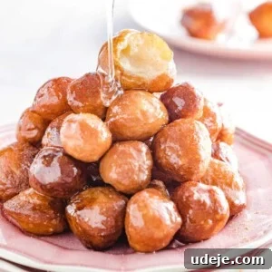 Luqaimat which is fried dough balls are stacked on a pink plate, bring drizzled by sugar syrup in a clear jug