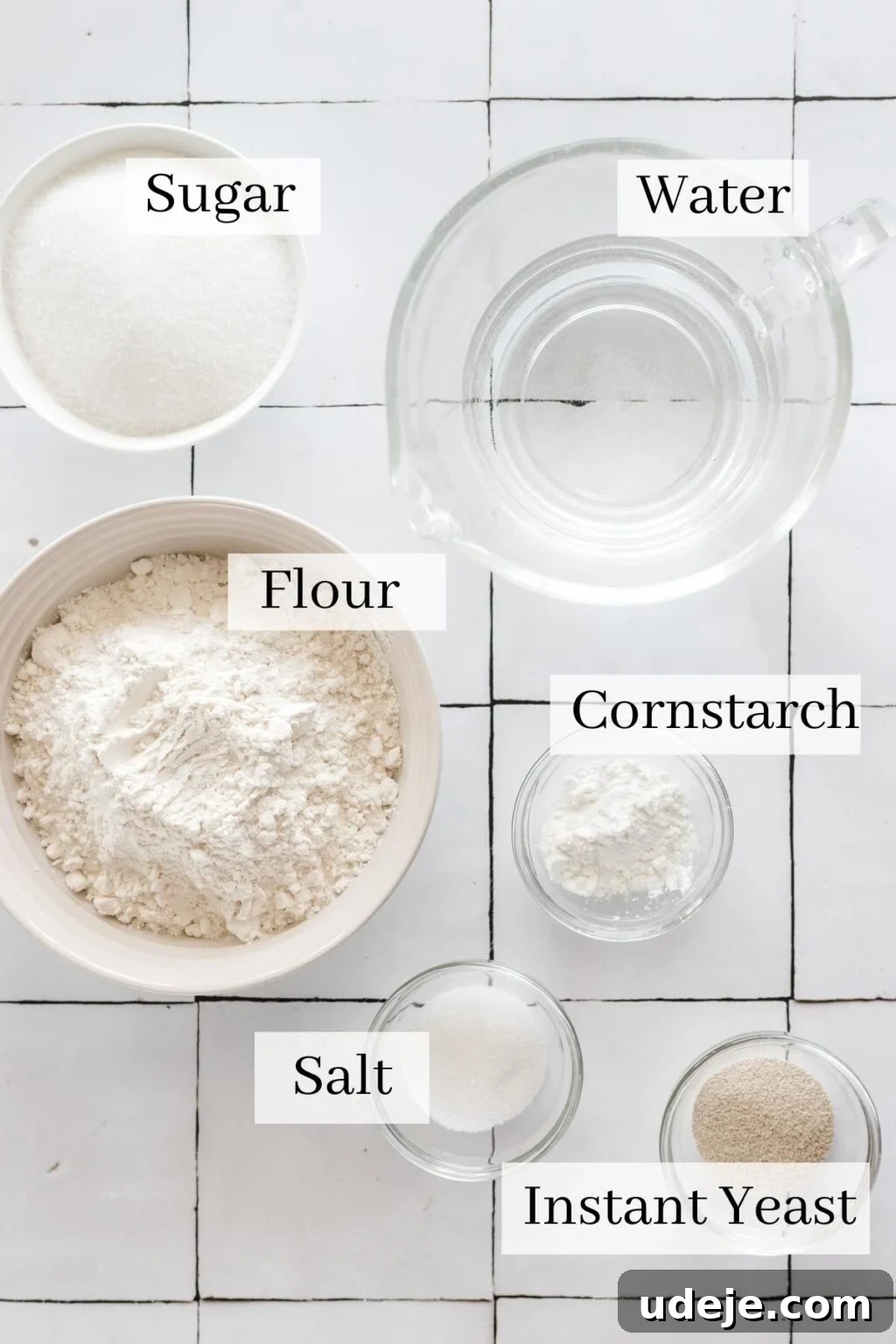 Crunchy Middle Eastern Luqaimat and Awamat Fritters 3 A vibrant collection of ingredients for making luqaimat, including neatly piled sugar, a clear glass of water, a bowl of all-purpose flour, a small bowl of cornstarch, a sprinkle of salt, and a sachet of instant yeast.