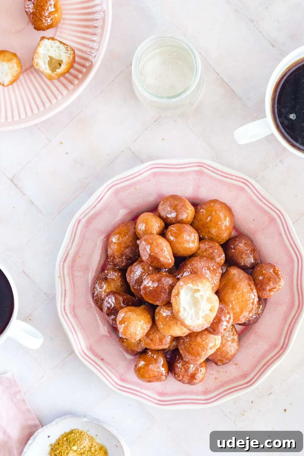 Crunchy Middle Eastern Luqaimat and Awamat Fritters 9 A delightful arrangement of golden Luqaimat (fried dough balls) stacked on a pink plate, accompanied by traditional coffee cups nearby, inviting a cozy and authentic Middle Eastern dessert experience.