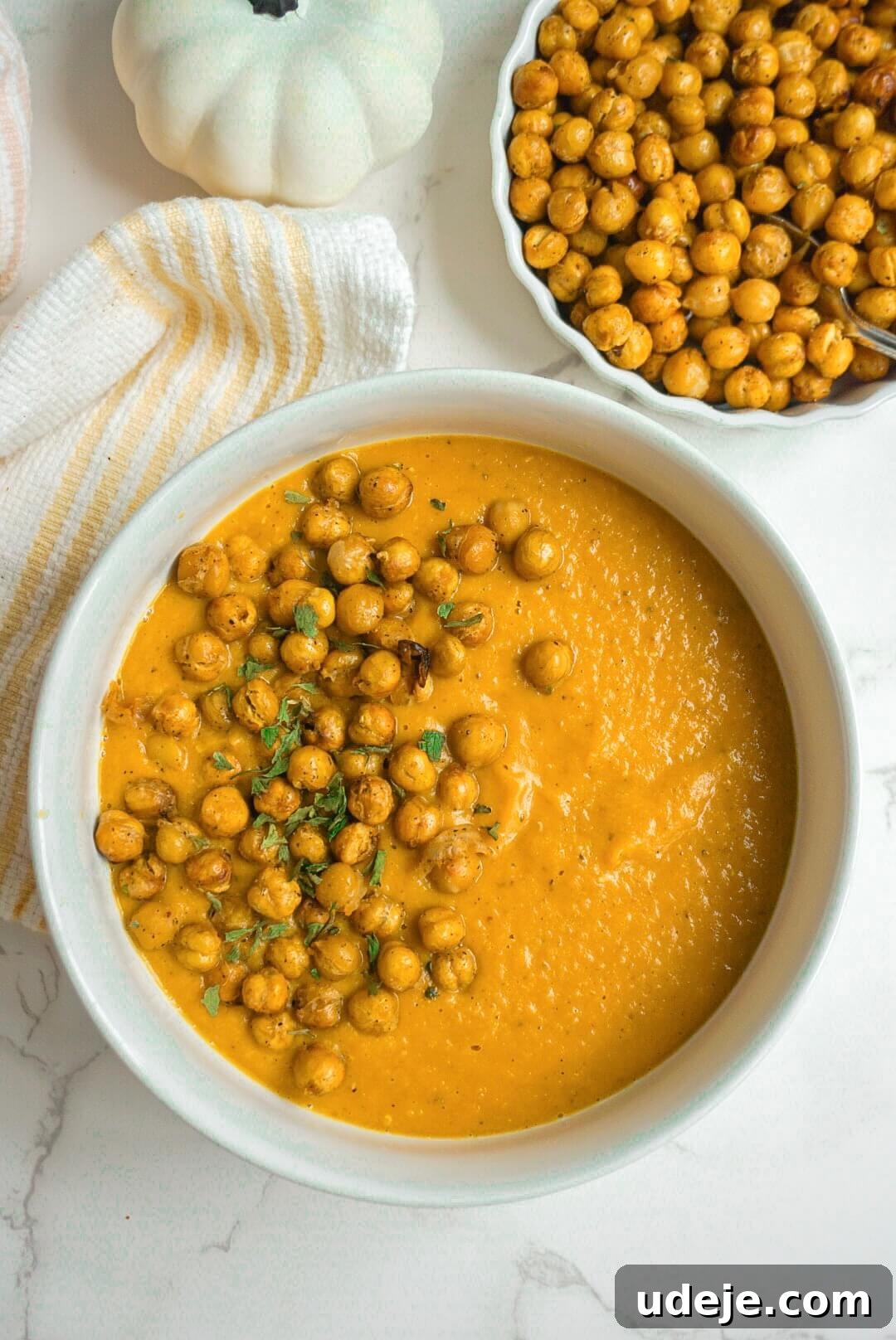 A warm, cozy, and wholesome Creamy Pumpkin Soup, filled with pumpkin puree and red lentils, topped with crispy chickpeas for protein and garnished with fresh herbs, perfect for the fall season.