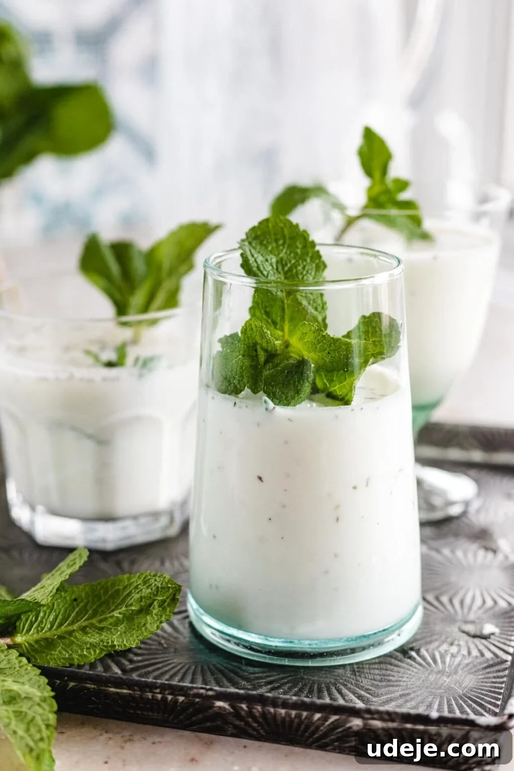Whip Up Refreshing Turkish Ayran in Just 5 Minutes 2 Several clear glasses filled with Ayran, a yogurt and mint drink, placed on a silver tray and topped with fresh mint.