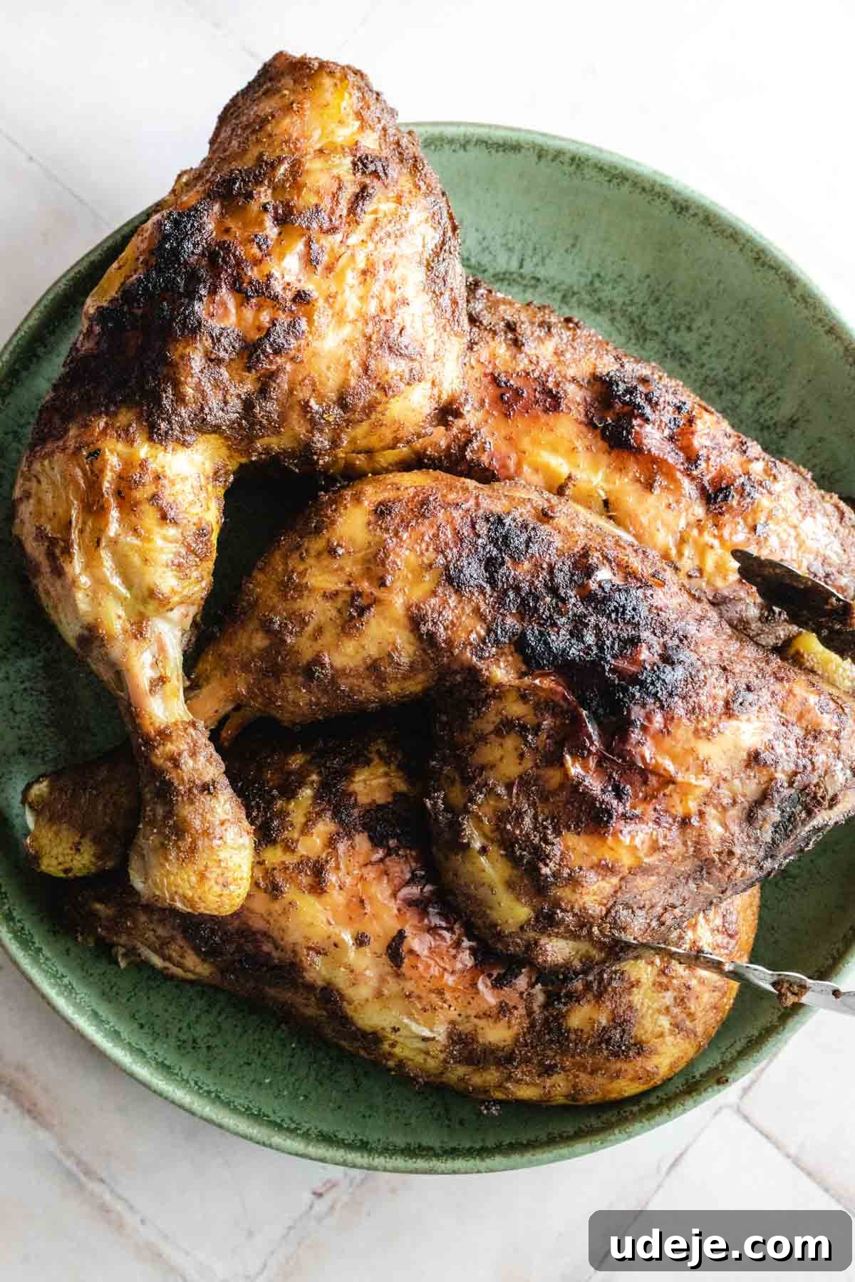 Yemeni Chicken Mandi with Fragrant Spiced Rice 12 Appetizing roasted chicken pieces layered in a green ceramic bowl, ready to be served with a serving spoon.