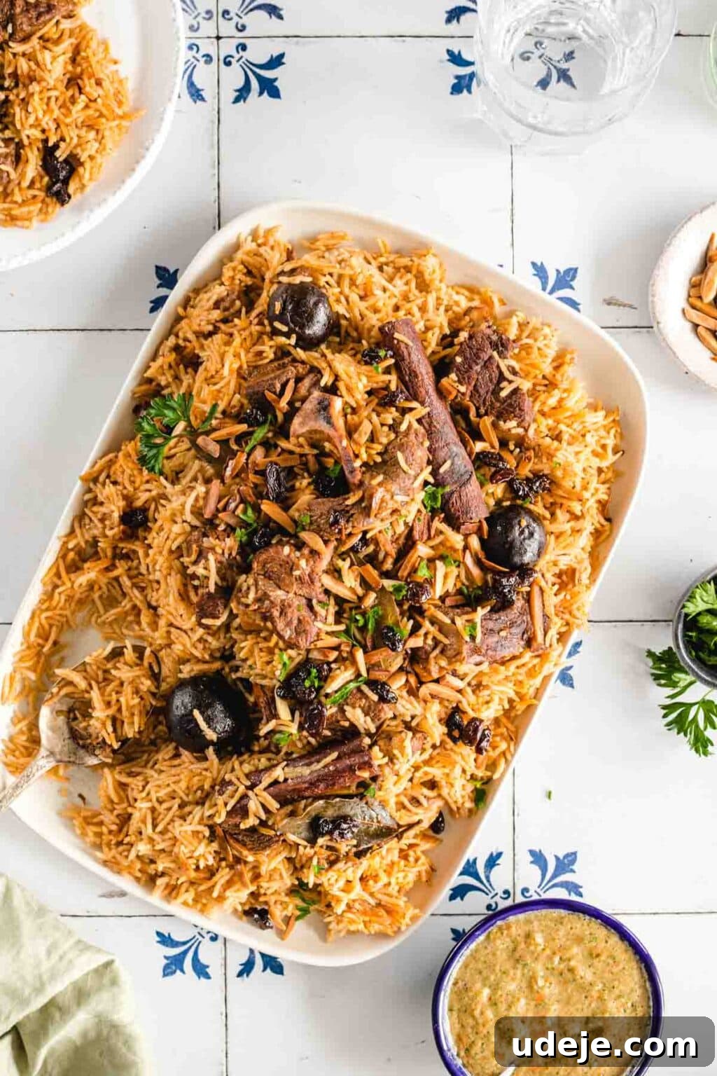 Chef's Signature Lamb Kabsa 2 Lamb and rice served on a white rectangle platter, with cilantro and salsa served nearby.