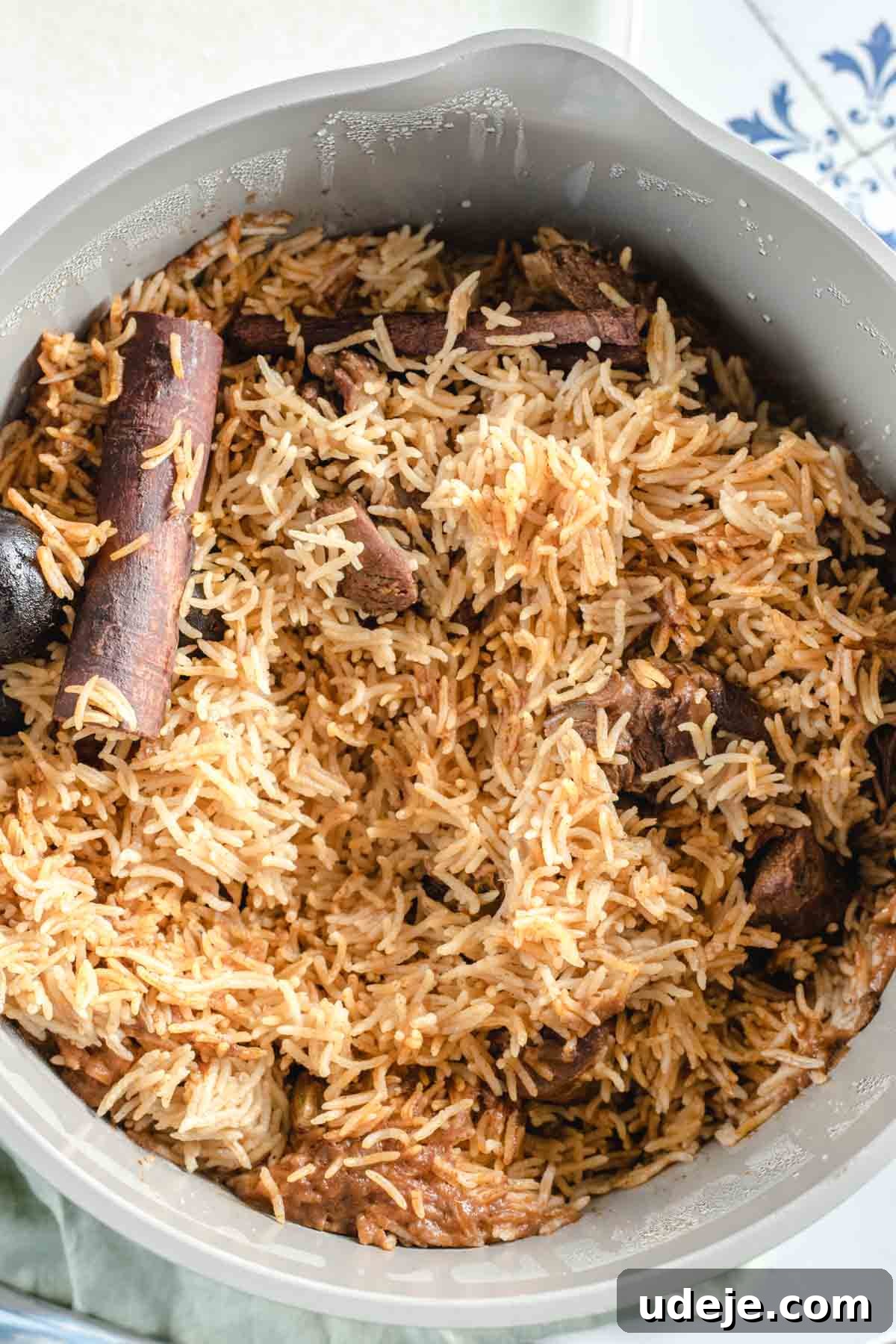 Chef's Signature Lamb Kabsa 13 A bowl filled with cooked spiced rice, visible chunks of lamb kabsa, and whole cinnamon sticks, showing fluffy rice grains mixed with brown, aromatic seasonings.